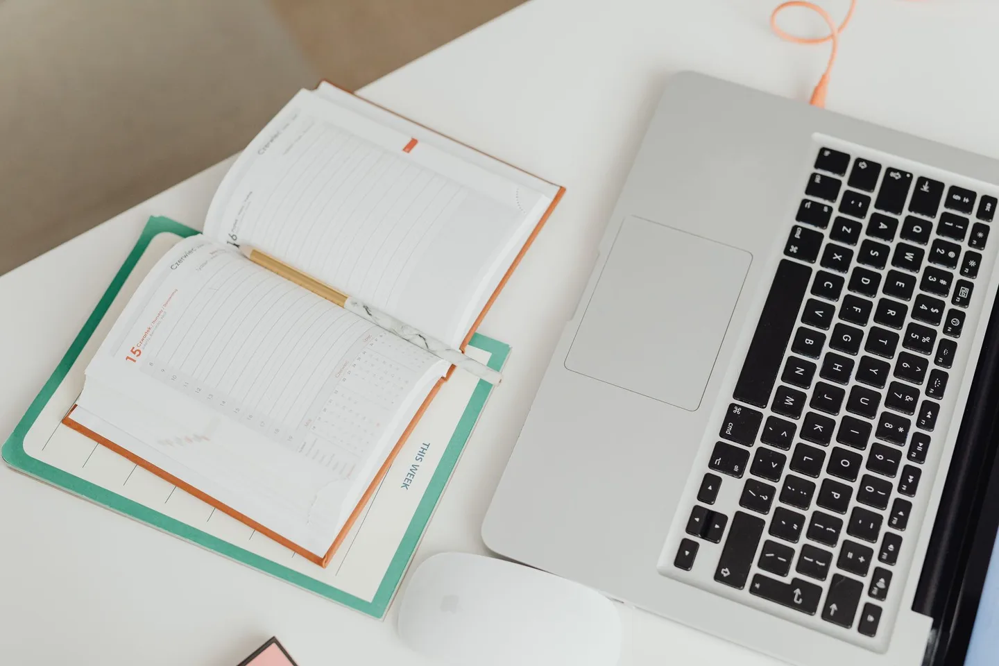 A notebook, laptop and mouse on a tidy white desk